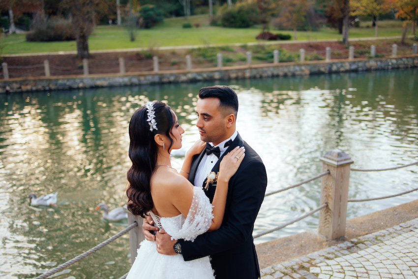 Zeynep’in gelinliği, kasrın taş duvarları arasında bir masal gibi süzülürken Ali’nin bakışlarında tek bir cümle vardı: “İyi ki.” Abartısız, gösterişsiz ama çok derin… İşte gerçek aşk tam da böyle bir şeydi. Poz vermek hiç gerekmedi; onlar yan yana durdukça anlar kendiliğinden oluştu. Gülüşler içtendi, dokunuşlar sakindi, her karede güven vardı. Hidiv Kasrı’ndaki çekim, hikâyenin ağırbaşlı başlangıcı gibiydi. Ardından Atatürk Arboretumu’na doğru yola çıktık. Sonbaharın sarıdan altına dönen renkleri, göl kenarında sessizce süzülen kuğular, yaprakların altında kalan patikalar… Doğa, sanki bu aşka özel hazırlanmıştı. Zeynep ve Ali yürüdükçe ışık onları takip etti, ağaçlar başlarını eğip bu mutluluğa tanıklık etti. Atatürk Arboretumu’nda çekilen her karede biraz huzur, biraz heyecan, çokça sevgi vardı. Gelinliğin etekleri yapraklara karıştı, kahkahalar dalların arasından yankılandı. Kimse acele etmedi. Çünkü bazı anlar çabuk geçmesin diye yavaş yaşanır. Benim için düğün fotoğrafçılığı, sadece güzel kareler yakalamak değil; o günün ruhunu, çiftlerin birbirine baktığında hissettiklerini yıllar sonrasına taşıyabilmek. Zeynep ve Ali çekim sonunda yanımdan ayrılırken yüzlerinde aynı ifade vardı: Hafiflemiş, mutlu ve tamamlanmış… İstanbul’da düğün fotoğrafı çektirmek isteyen her çift için Hidiv Kasrı ve Atatürk Arboretumu hâlâ en özel duraklardan. Ama asıl güzellik, oraya götürdüğünüz hikâyede saklı. Doğru ışık, doğru an ve samimi bir bağ bir araya geldiğinde ortaya çıkan şey, sadece fotoğraf değil; bir hatıradır.