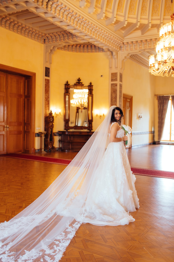 Adile Sultan Kasrı büyük salonunda avizenin altında poz veren İmran ve Burak düğün fotoğraf çekimi